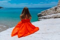 Beautiful young girl by the sea. Woman in a red dress on the beach. Seaside vacation. Rocky terrain Royalty Free Stock Photo