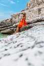 Beautiful young girl by the sea. Woman in a red dress on the beach. Seaside vacation. Rocky terrain Royalty Free Stock Photo