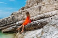 Beautiful young girl by the sea. Woman in a red dress on the beach. Seaside vacation. Rocky terrain Royalty Free Stock Photo