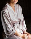 Beautiful young girl in silk robe sitting on chair and crosses.