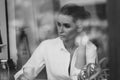 A beautiful young girl sits in a cafe behind a glass with a cup of coffee and looks thoughtfully out the window. Black and white Royalty Free Stock Photo