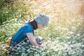 A beautiful young girl sits in a daisy field - a summer photograph in the backlight, sunny.