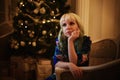 Beautiful young girl sits on sofa near Christmas tree with presents and dreams Royalty Free Stock Photo