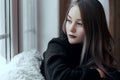 Beautiful young girl sitting alone on the windowsill and looking out the window Royalty Free Stock Photo