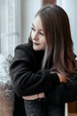 Beautiful young girl sitting alone on the windowsill and looking out the window Royalty Free Stock Photo