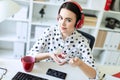 Beautiful young girl sitting in headphones at desk in office eating yogurt with red filling.