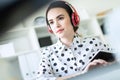 Beautiful young girl sitting in headphones at desk in office. Photo with depth of field, focus on girl.