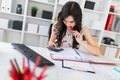 Beautiful young girl sitting at an office desk holding a pen in her mouth and looking into the calculator. Royalty Free Stock Photo