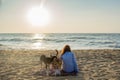 Beautiful young girl sitting on the towel at the beach with two dogs playing around during sunset Royalty Free Stock Photo