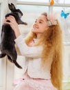 Beautiful young girl sitting on a windowsill and playing with Easter bunny. Royalty Free Stock Photo