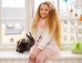 Beautiful young girl sitting on a windowsill and playing with Easter bunny. Royalty Free Stock Photo