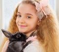 Beautiful young girl sitting on a windowsill and playing with Easter bunny. Royalty Free Stock Photo
