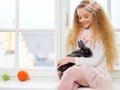 Beautiful young girl sitting on a windowsill and playing with Easter bunny. Royalty Free Stock Photo