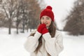 Beautiful young girl smiles straight into camera, in wool red hat and mittens. Woman in knitted clothes in winter park Royalty Free Stock Photo