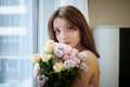 Beautiful young girl standing near the window with a bouquet of flowers and looking at the camera, indoors female Royalty Free Stock Photo