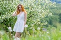 Beautiful and young girl standing next to a blooming Apple tree in a white dress. Red lips of the girl Royalty Free Stock Photo