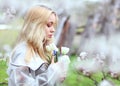 A girl with white hair, in a transparent jacket, stands near a blossoming tree with white tulips. Spring mood