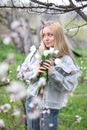 A girl with white hair, in a transparent jacket, stands near a blossoming tree with white tulips. Spring mood