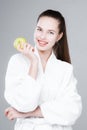 A beautiful young girl stands on a light background holding an apple in her hand, smiling Royalty Free Stock Photo