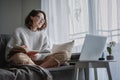 Beautiful young girl student studying at home online while sitting in a warm sweater on the couch in front of a laptop making