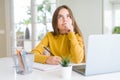 Beautiful young girl studying using computer laptop and writing on notebook serious face thinking about question, very confused Royalty Free Stock Photo