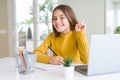 Beautiful young girl studying using computer laptop and writing on notebook surprised with an idea or question pointing finger Royalty Free Stock Photo