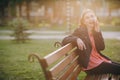 Beautiful young girl talking on the phone sitting on a bench in the city park. Young woman dressed in stylish wear Royalty Free Stock Photo