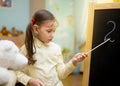 Beautiful young girl is teaching toys at home on blackboard. Preschool home education. Royalty Free Stock Photo
