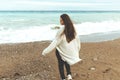 A beautiful young girl walks along the seashore, a storm, hair fly apart, a gray cardigan, a sports figure in sneakers Royalty Free Stock Photo