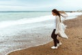 A beautiful young girl walks along the seashore, a storm, hair fly apart, a gray cardigan, a sports figure in sneakers Royalty Free Stock Photo