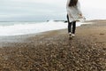 A beautiful young girl walks along the seashore, a storm, hair fly apart, a gray cardigan, a sports figure in sneakers Royalty Free Stock Photo