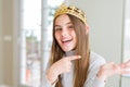 Beautiful young girl wearing a golden crown as a princess from fairytale amazed and smiling to the camera while presenting with Royalty Free Stock Photo