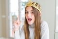 Beautiful young girl wearing a golden crown as a princess from fairytale pointing finger up with successful idea