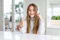 Beautiful young girl wearing headphones listening to music and dancing happy with big smile doing ok sign, thumb up with fingers, Royalty Free Stock Photo