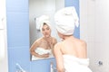 A beautiful young girl in a white bath towel on her head and body in the bathroom looks at her face. Hygiene Royalty Free Stock Photo