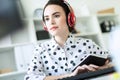 Beautiful young girl sitting in headphones at desk in office. Photo with depth of field, focus on girl.