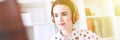 Beautiful young girl sits in headphones at desk in office, holds a notebook in her hand and prints on the keyboard