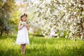 Beautiful young girl in white dress in the garden with blosoming apple trees. Cute girl holding apple-tree branch