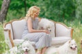 Beautiful young girl with a white puppy in her arms and older white fluffy dogs on a retro sofa in a summer garden Royalty Free Stock Photo