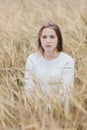 Beautiful young girl in a white sweater sits in a wheat field