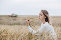 Beautiful young girl in a white sweater sits in a wheat field and holds ears of wheat in his hand.