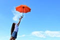 beautiful young girl white T-shirt and denim shorts throws up an orange umbrella. A flying umbrella against the blue summer sky. A Royalty Free Stock Photo