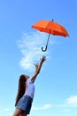 beautiful young girl in a white T-shirt and denim shorts throws up an orange umbrella. A flying umbrella against the blue summer Royalty Free Stock Photo