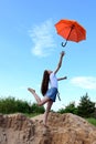 beautiful young girl in white T-shirt and denim shorts throws up an orange umbrella. Sunny summer day outdoors on blue sky Royalty Free Stock Photo