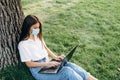 Beautiful and young girl who studies and works with a laptop with a surgical mask in the park, blogger and smart worker during the