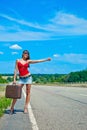 Beautiful young girl or woman in mini with suitcase hitchhiking along a road Royalty Free Stock Photo