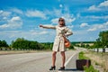 Beautiful young girl or woman in mini with suitcase hitchhiking along a road - retro style Royalty Free Stock Photo