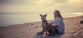 Beautiful young girl woman sitting on the beach in the sand with her dog and watching the beautiful sunset Royalty Free Stock Photo