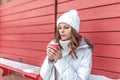 Beautiful and young girl, a woman in winter in a warm jacket and hat, holding a cup of coffee tea, is warmed by a hot Royalty Free Stock Photo