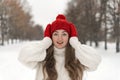 Beautiful young girl in wool red hat and mittens smiles straight into camera. Woman in knitted clothes in winter forest Royalty Free Stock Photo